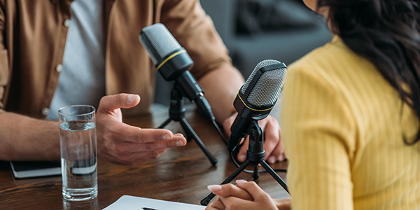 Two individuals discussing a topic at a podcast setup with mics pointed at themselves.